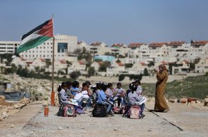 A teacher gives a class to Palestinian bedouin students outdoors near the Jewish settlement of Maale Adumim (seen in the background), in the West Bank village of Al-Eizariya, east of Jerusalem. Photo: UNI