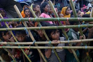 Rohingya refugees look through a fence as they wait outside of aid distribution premises at a refugee camp. Photo: UNI