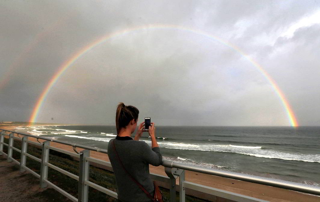 LIGHT ARCH: A woman takes a picture of rainbow appearing off the coast of Sydney's Wanda Beach in Australia, as the setting sun illuminates a passing rain shower, Reuters/UNI