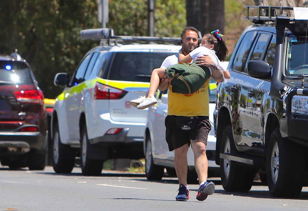 HELPING HANDS: A man carries a child near where a vehicle crashed into a primary school classroom in the Sydney suburb of Greenacre in Australia, Paul Braven/AAP/Reuters/UNI